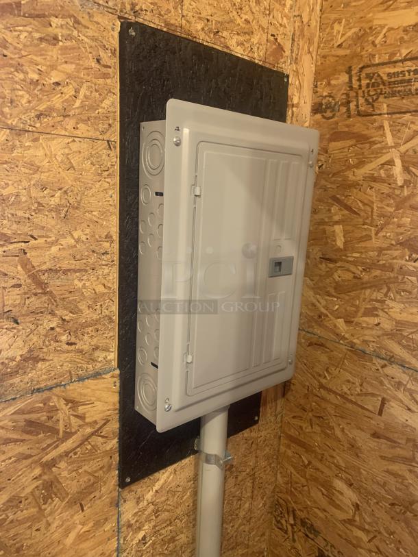Electrical breaker box mounted on plywood panel, new condition, featuring a closed metal door and conduit connection.