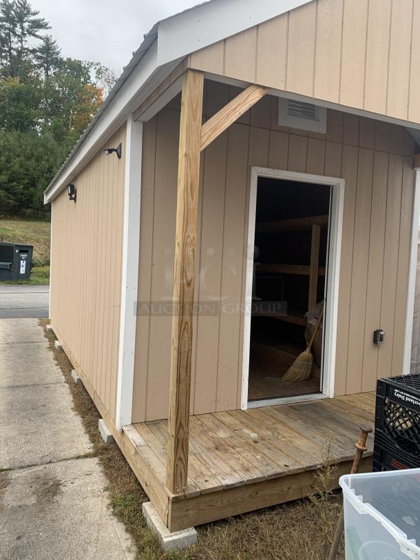 Tan wooden shed with white trim, open door, front porch, and small light fixtures. Good condition, outdoor setting.