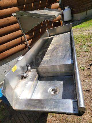 Stainless steel outdoor sink with two compartments, faucet, and drainage. Features shelves and a yellow safety label. Used condition.