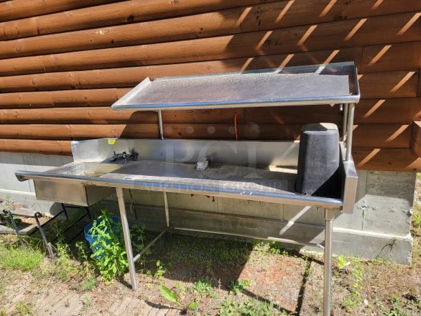 Stainless steel outdoor sink with single faucet, side basin, and shelf. Weathered condition. Ideal for outdoor use.