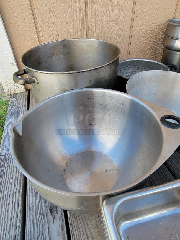 Assorted stainless steel and aluminum commercial cookware, including large pots and pans, suitable for restaurant use.