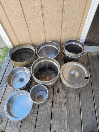 Assorted stainless steel pots and containers on wooden surface, ideal for camping or outdoor cooking. Slightly used condition.