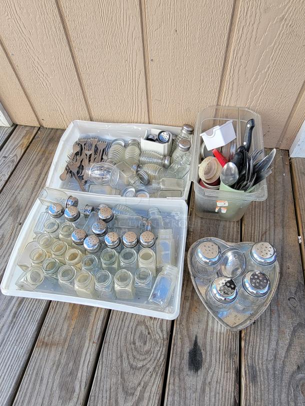 Assortment of kitchenware including spice jars, cutlery, and utensils in bins on a wooden surface. Ideal for organization and meal prep.