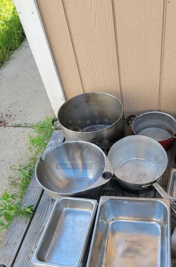 Assorted stainless steel and aluminum cookware, including pots, pans, and trays, ideal for commercial kitchen use.