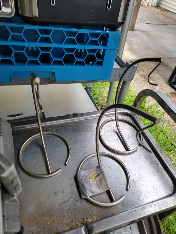 Assorted commercial kitchen lot featuring metal banana holders, blue plastic tray, and stainless surfaces. Visible wear.