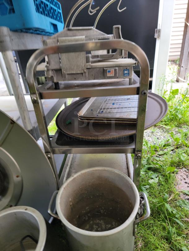 Assorted commercial kitchen lot with metal vegetable slicer, trays, and cooking pots on a rack. Used condition.