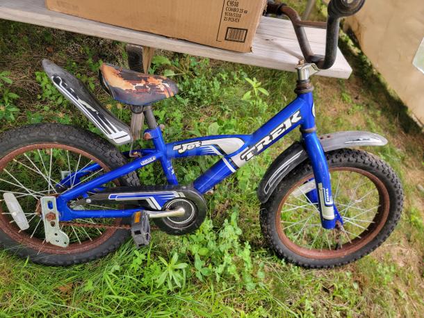 Blue Trek child's bicycle with rusted wheels and worn seat, part of a children's outdoor toy set.