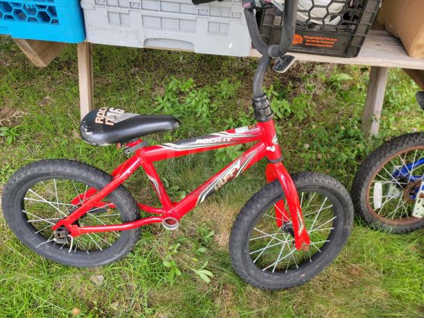 Red Huffy Rock It children's bicycle with black seat and handlebar, in good condition, on grassy area.