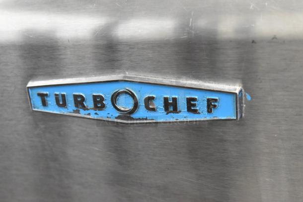 Close-up of a Turbochef logo on a commercial electric HhC2020 rapid cook conveyor oven. Stainless steel surface.