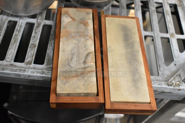 Two sharpening stones with wooden bases, showing varied wear and natural stone patterns.