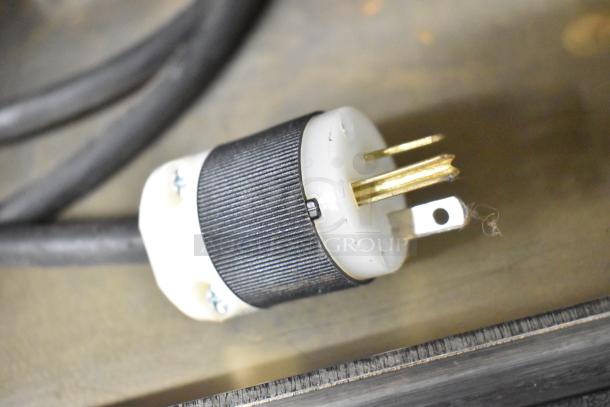 Close-up of a three-prong electrical plug connected to a cable, shown on a flat surface.