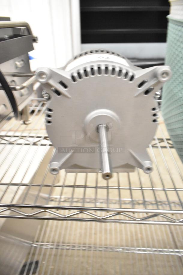 Brand new Nidec motor, scratch and dent condition. 208-240 volts, 1 phase. Silver casing, visible shaft, on metal shelf.