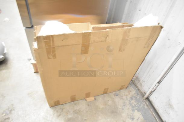 Cardboard box containing four brand new scratch and dent items: Bon Chef 52109 EX Fit Tile Pattern Tabletop, box of legs, and metal oven racks.