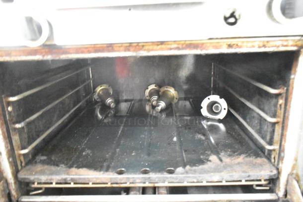 Garland stainless steel gas-powered vertical upright broiler, commercial, interior view. Signs of use, visible burners and racks.