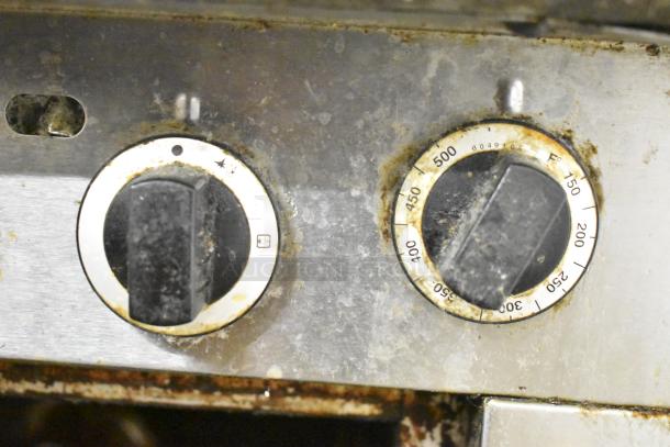 Close-up of Garland stainless steel commercial gas broiler controls showing temperature dials in used condition.