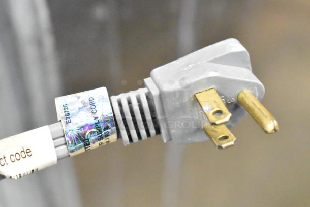 Close-up of Scotsman C0322SA-1B ice machine's power cord plug, showing three prongs and a label indicating a power supply.