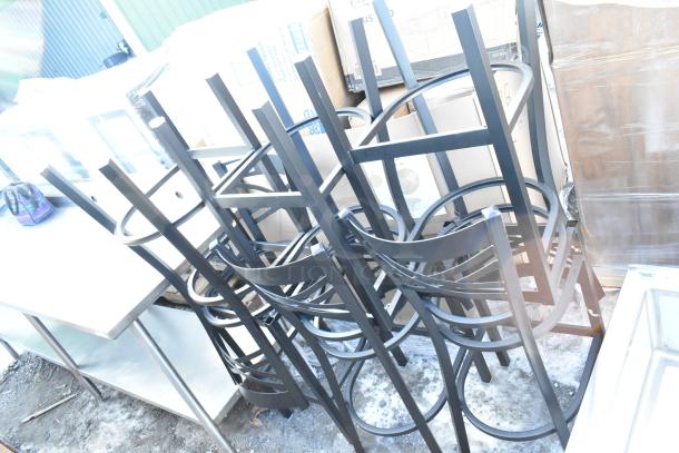 Six new black metal cross back bar height chair frames, slightly scratched, stacked together outdoors.