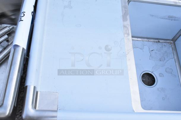 Brand new Regency 600S3182418L stainless steel 3 bay sink with a left-side drain board, visible scratches and dents, missing legs.