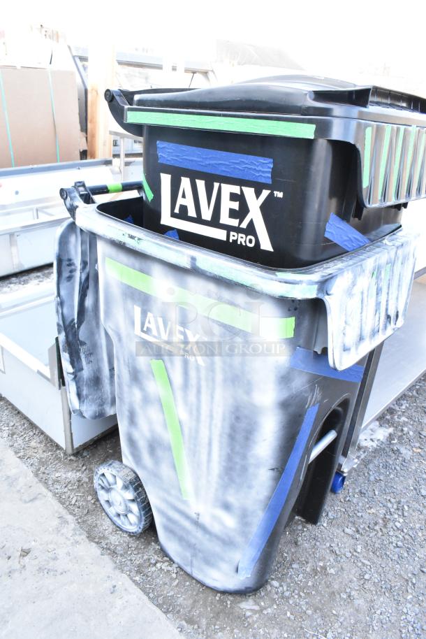 Two Lavex Pro black poly trash cans, brand new with minor scratches and dents, featuring durable wheels and attached lids.