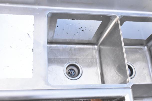 Regency 600S3141414C stainless steel L-shaped 3-bay sink with dual drain boards, new scratch and dent, no legs visible.