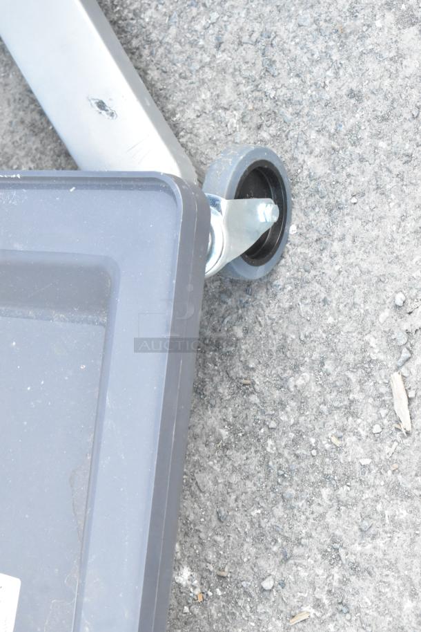 Dish caddy dolly with a metal frame and caster wheels on asphalt surface; wear visible.