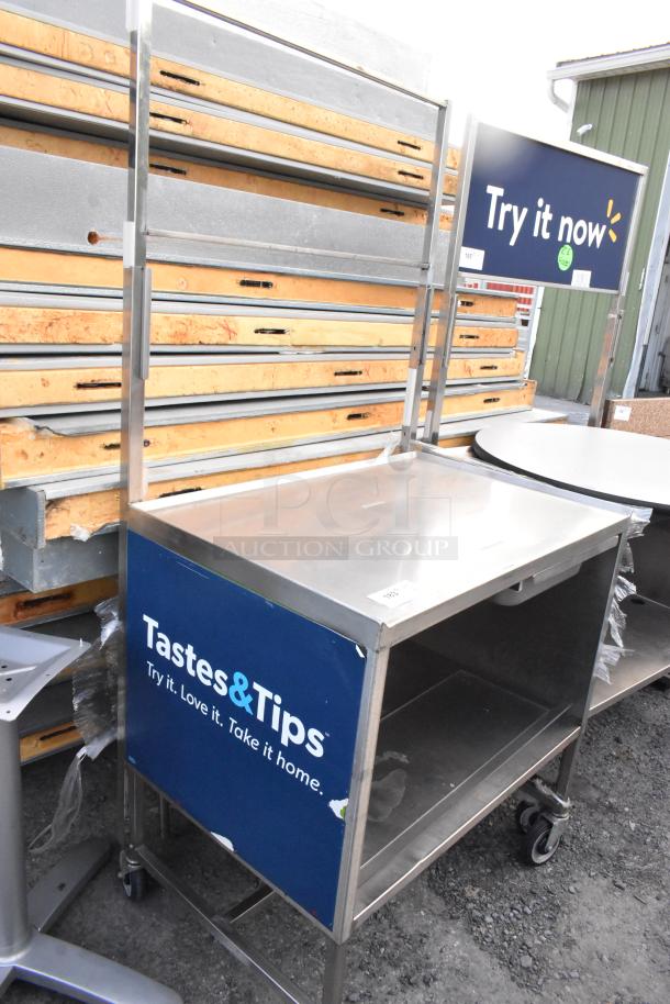 Stainless steel table with under shelf and drawer, on commercial casters. Features "Tastes&Tips" sign. Good condition.