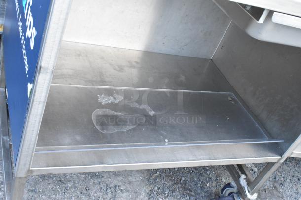 Stainless steel table with under shelf and drawer, on commercial casters, minor surface stains, sturdy and functional.