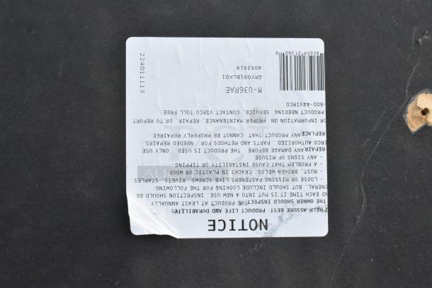 Round tabletop in dark material, with a visible manufacturer's notice label detailing maintenance instructions and product information. Small hole marks present.
