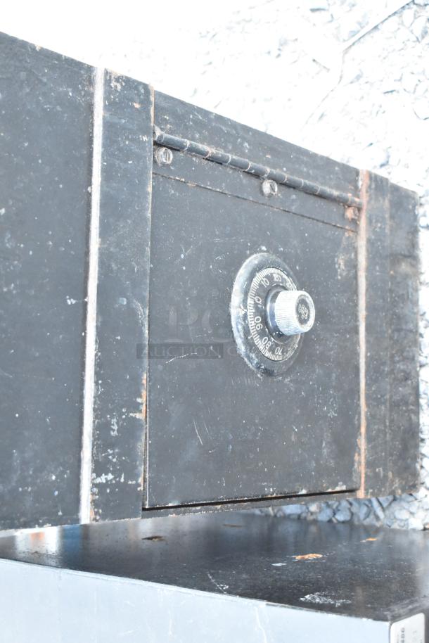 Black metal single compartment safe with a combination dial. Visible wear, no combination provided.