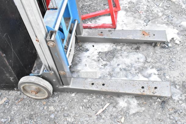 Genie Lift hand-operated lift truck with visible rust on metal parts, sturdy wheels, blue and gray frame, outdoor condition.