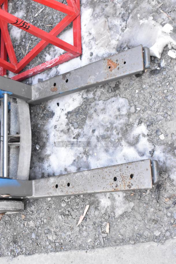 Genie Lift Hand Operated Lift Truck showing rust on metal forks and wheels, used condition, with a red framework visible.