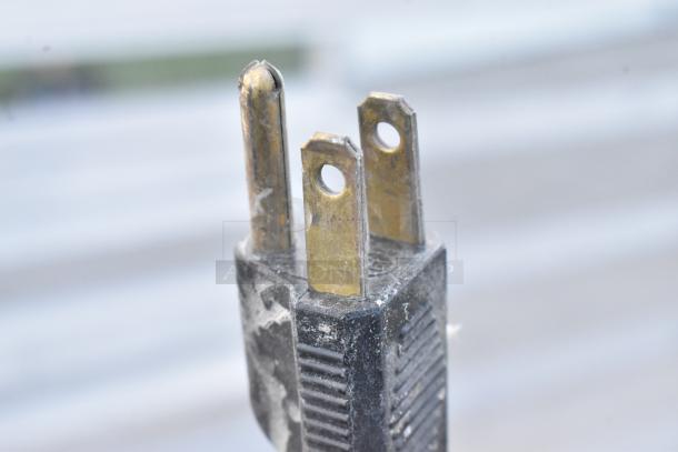 Close-up of a three-pronged plug for a Karma 104 countertop chocolate warmer, showing metallic prongs and a black plastic casing.