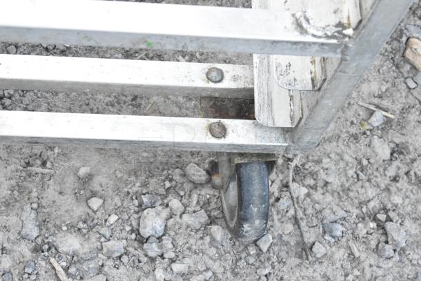 Commercial pan transport rack with sturdy metal frame, featuring commercial casters for mobility. Visible wear and rust marks.