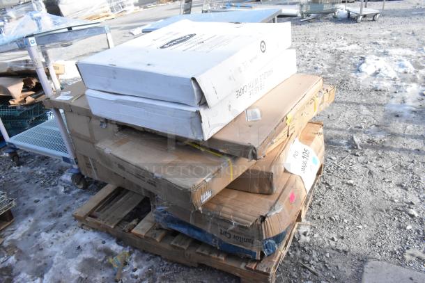 Stack of boxes on a pallet with visible scratch and dent labels, including brands like Kohler, in new condition.