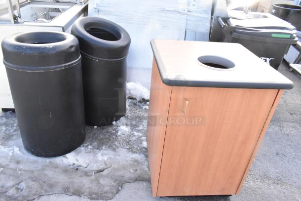 Three trash cans, including a wooden shell with black top and two black cans; sturdy construction, minor wear.