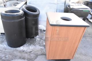 Three trash cans, including a wooden shell with black top and two black cans; sturdy construction, minor wear.