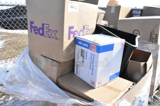 Boxes containing a variety of scratched and dented items, including hot cups and trash cans, stacked near a chain-link fence.