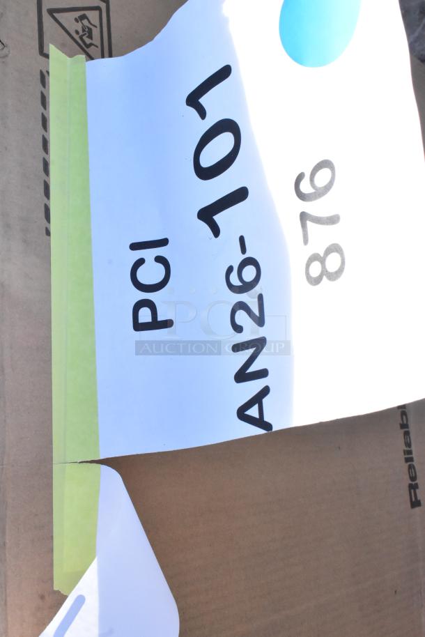 Cardboard box with partial view of labels displaying "PCI AN26-101" and "876." Labels attached with green tape. Box condition appears intact.
