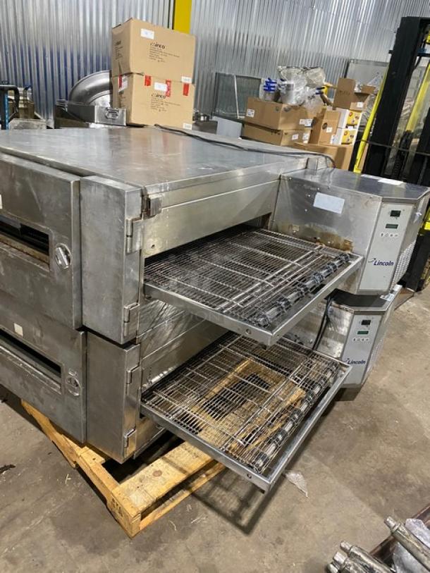 Lincoln conveyor pizza oven, stainless steel, dual deck, visible wear, digital controls, on pallet, industrial setting.