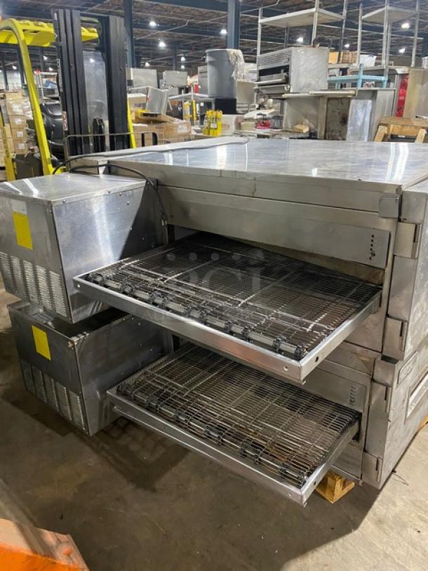 Conveyor pizza oven with dual stacked chambers, stainless steel exterior, used condition. Visible power units, no labels.