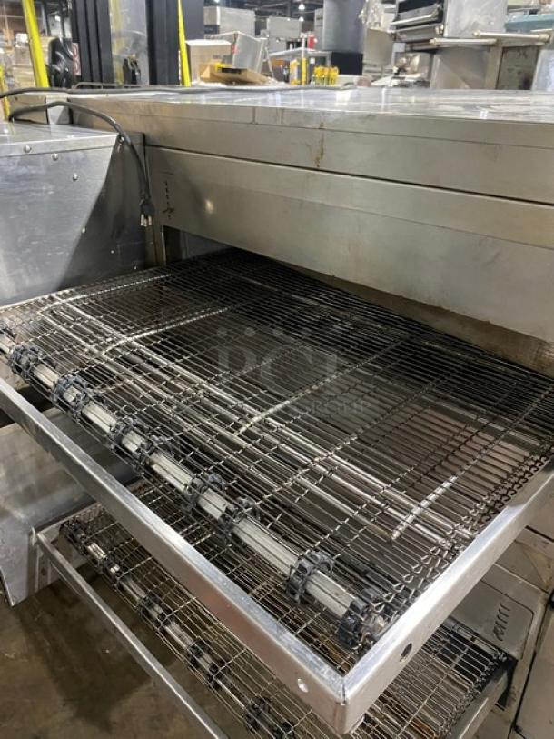 Commercial conveyor pizza oven, stainless steel, used condition, visible wear. Features rotating conveyor belt for efficient cooking.