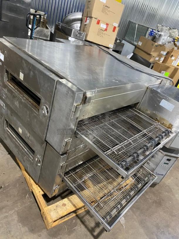 Commercial conveyor pizza oven, stainless steel, dual decks, visible wear, no identifiable brand markings, includes conveyor racks.