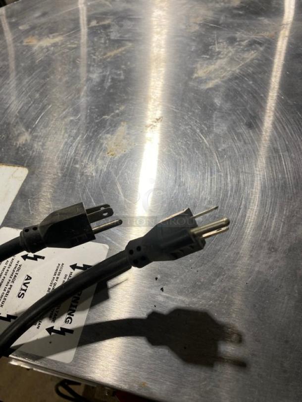Black power cords with standard three-prong plugs, resting on a metal surface. Visible warning label in background.