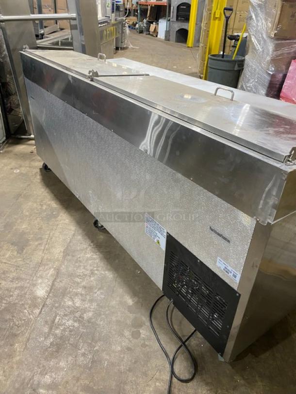 Commercial stainless steel refrigerator with caster wheels, featuring a top-access panel. Visible brand and model label. Used condition.