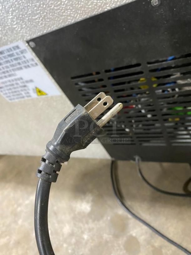Power cord for an electrical device, showing a standard two-prong plug. Background includes a vented panel and a label with technical specifications. Used condition.