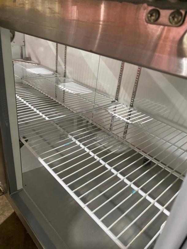 Commercial stainless steel display fridge with wire shelving, clean interior, and adjustable shelving brackets. Good condition.