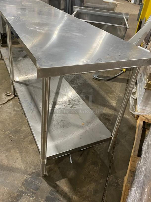 Stainless steel work table with lower shelf, industrial-grade, shows some surface wear. Ideal for kitchen or workspace use.