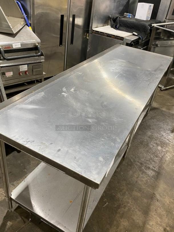 Stainless steel commercial kitchen prep table with lower shelf; shows mild wear and scratches; durable and spacious.