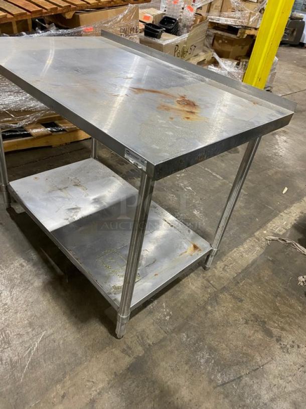 Industrial stainless steel table with two shelves, showing signs of rust and wear, in a warehouse setting.