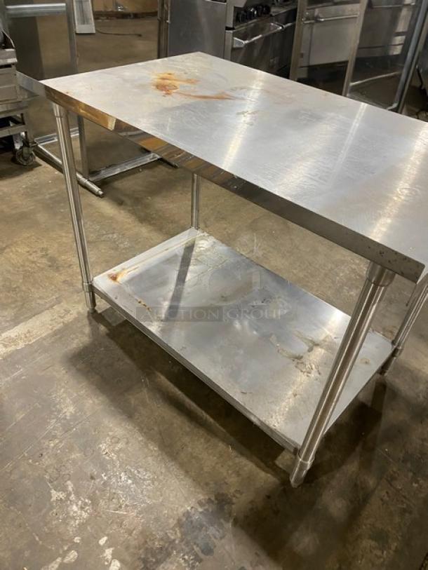 Stainless steel work table with two shelves, showing signs of rust and wear. Ideal for industrial or kitchen use.